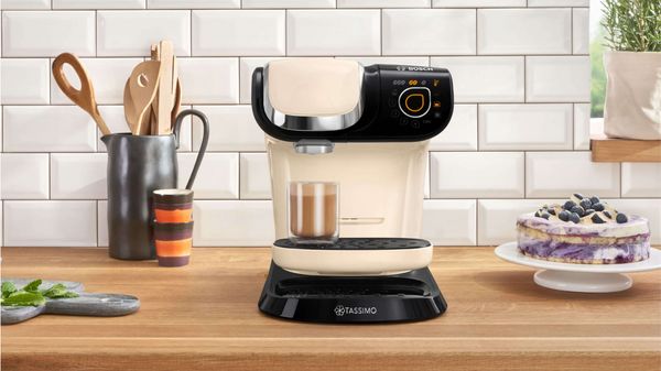The TASSIMO coffee machine MYWAY 2 standing with a Cortado on a kitchen worktop and a cake next to it.