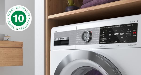 Free-standing Bosch washing machine with folded laundry on top. 10-year warranty icon at the left symbolises the free extended warranty on the motor.
