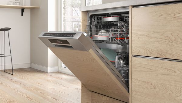 An open semi-integrated built-in dishwasher in a wooden cabinet.