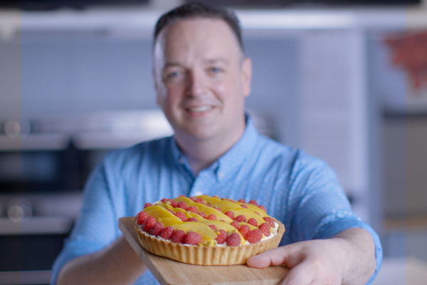 The Cupcake Bloke holding a raspberry, passion fruit & mango tart