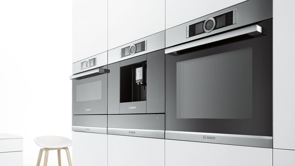 Dos hornos y una máquina de café integrados en un armario blanco en una cocina blanca.