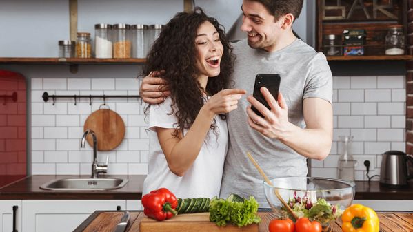 Un couple debout dans la cuisine regarde un téléphone intelligent.