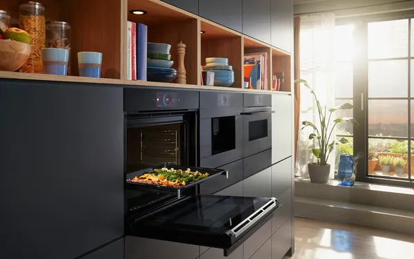 Cuisine élégante avec four intégrable Série 8 de Bosch avec fonction Air Fry et tiroir culinaire chauffant. Cuisson de différents légumes au four. Plus de légumes sur une planche à découper déposée sur un comptoir.