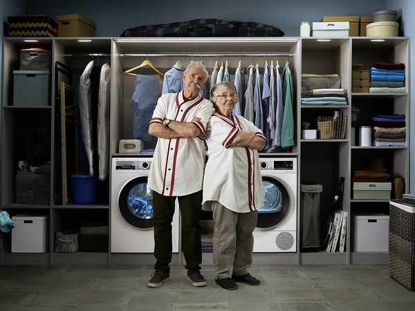 Two elderly people proudly standing in front of their washing machine and heat pump dryer. Both of them wearing the same sports jersey.