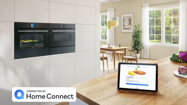 Elegant kitchen with built-in Series 8 built-in electric oven and warming drawer. A tablet computer on the counter shows Home Connect App.