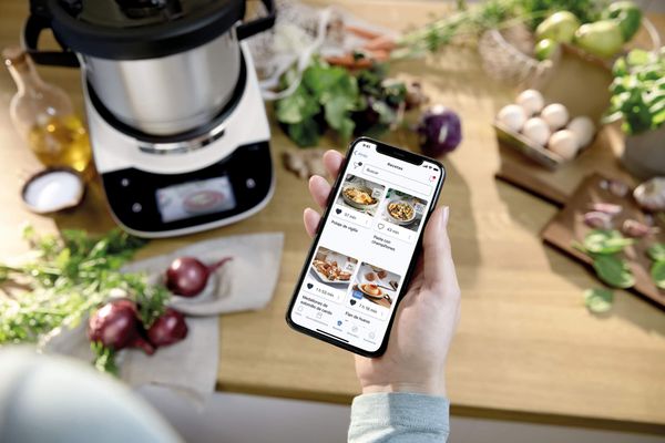 Auf einem Smartphone geöffnete Home Connect App vor einem Cookit. 