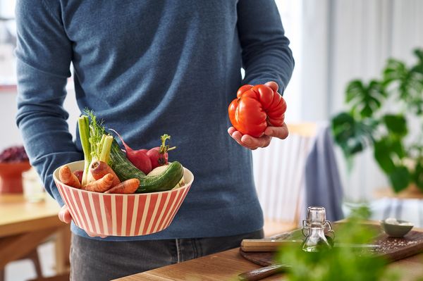 Mann hält eine Schüssel voll Gemüse und eine deformierte Tomate in den Händen.