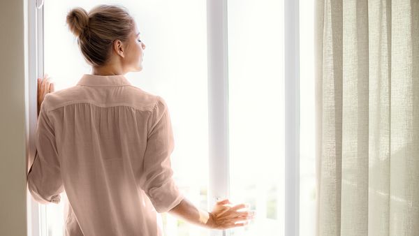 En kvinne står ved et åpent vindu og nyter den friske luften.