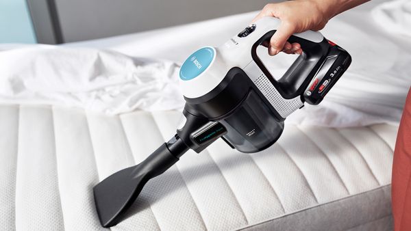 Et spesielt madrassmunnstykke er festet til Unlimited 7 ProHygienic Aqua. En person bruker det til å støvsuge overflaten på en madrass.