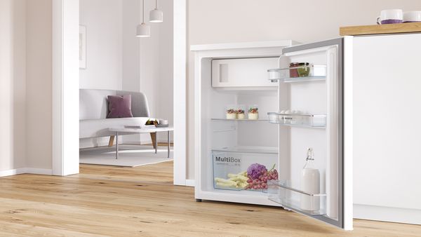 The door of a mini fridge stands ajar, revealing a freezer compartment and stocked shelves.
