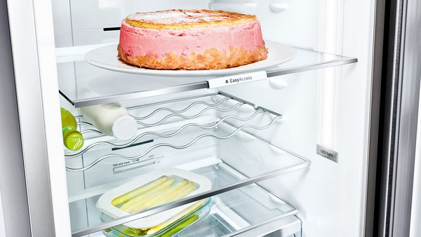Open refrigerator with a cake on a flexible glass shelve.