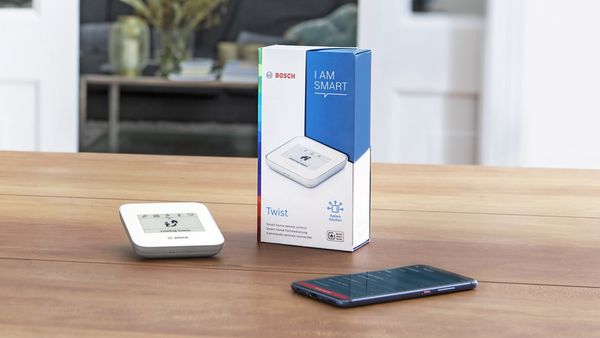 Ein iPhone und eine Verpackung des Bosch Smart Twist Controllers, sowie das Gerät selbst liegen auf einem Holztisch.