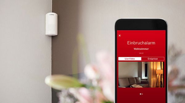 Der Bosch Smart Home Bewegungsmelder und ein Handy mit der Smart Home App, der aktuelle Infos aus der Wohnung zeigt.
