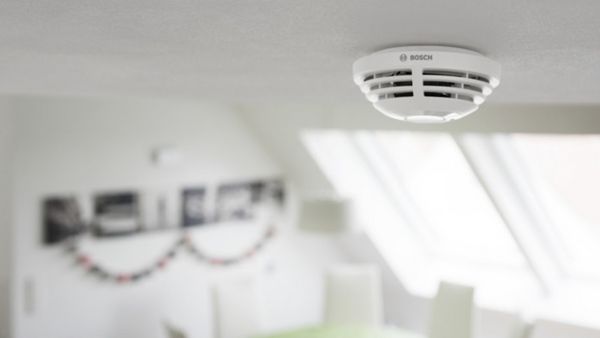 Der Bosch Smart Home Rauchwarnmelder, der an der Decke eines weißen Zimmers montiert ist.