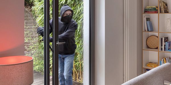 Ein vermummter Einbrecher, der über die Terassentüre in ein Haus eindringt.