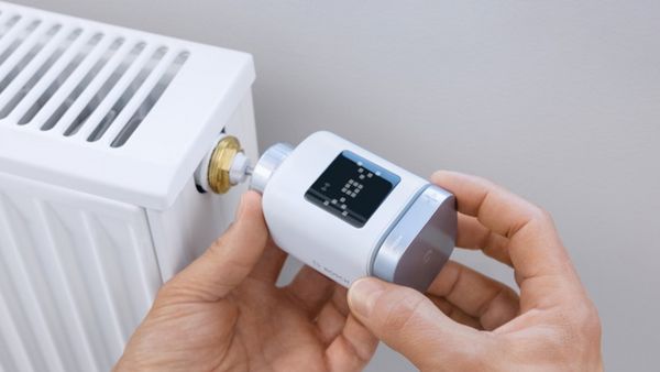 Close up von einem smarten Heizkörper-Thermostat, der mit zwei Händen an die Heizung montiert wird.