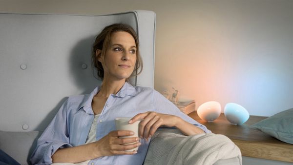 Eine Frau, die gemütlich auf einem Sessel sitzt neben einem kleinen Wandregal mit Bosch Smart Home Lampen.