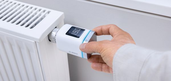 Ein Mann stellt die Temperatur an einem digitalen Thermostat einer Heizung ein. 