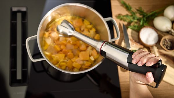 Une femme réduit des légumes en purée pour obtenir une soupe crémeuse à l'aide d'un mixeur plongeant ErgoMaster Bosch.