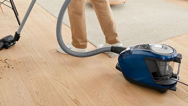 A person picks up debris off a hardwood floor with a Bosch bagless vacuum.