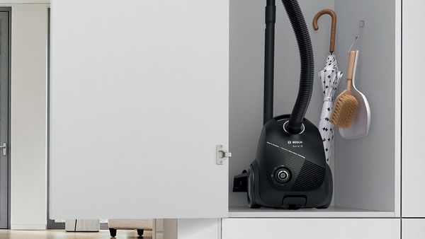 Un aspirator super-compact Bosch cu sac este depozitat cu ușurință într-un dulap împreună cu o umbrelă și cu alte obiecte folosite la curățenie.