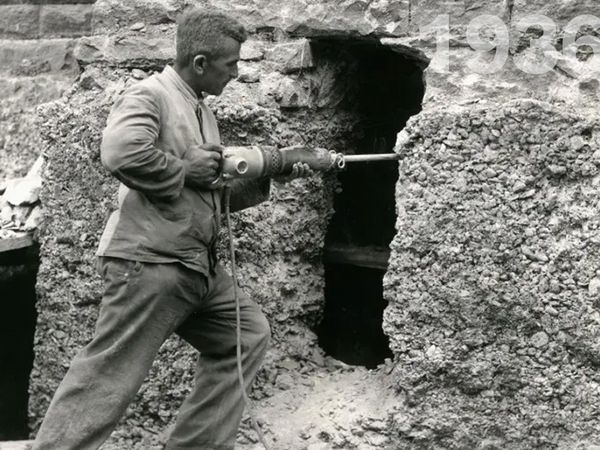 Ein Mann im Jahre 1936 stemmt gerade eine Wand mit einem Bohrhammer auf.