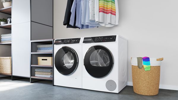 Una lavadora Serie 8 y una secadora con bomba de calor Serie 8 una al lado de la otra en una habitación con prendas colgadas en la parte superior.