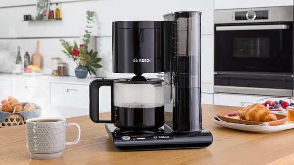 Filter coffee machine with semi-filled carafe of coffee next to cup on kitchen counter.