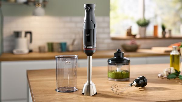 A Bosch hand blender, smoothie in a beaker and plates of food on a kitchen counter.