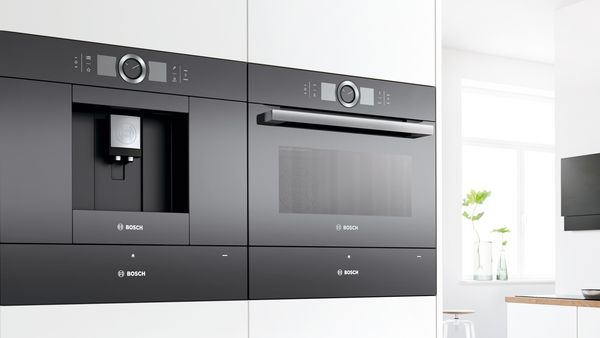 Built-in coffee machine next to built-in oven in a white interior kitchen.