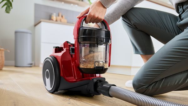 A person lifts the dust box out of a bagless canister vacuum.