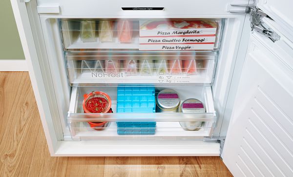 Prezentare a unui compartiment congelator deschis, fără depuneri de gheaţă, plin cu alimente şi iluminat.