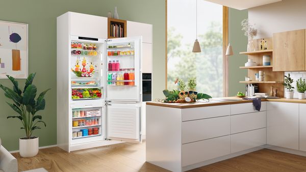Total view of a kitchen-dining area in a beautiful modern built-in kitchen with an open XXL fridge freezer. The fridge contains a beautiful pirate ship made out of fruits.