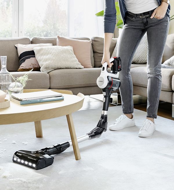 Woman cleans the kitchen floor with a flexible cordless Unlimited vacuum.