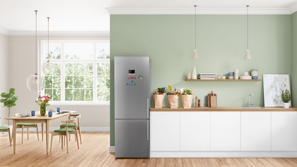 Ubicado junto a un mostrador y cerca de una mesa y sillas, un frigorífico XL independiente es el corazón de una cocina luminosa y soleada.
