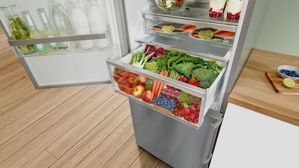 El cajón VitaFresh completamente extendido dentro de un refrigerador grande está repleto de deliciosas frutas y verduras frescas.