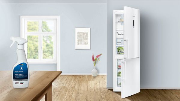 Halvt åbent køleskab og rengøringsmiddel til køleskabe på et bord. 
