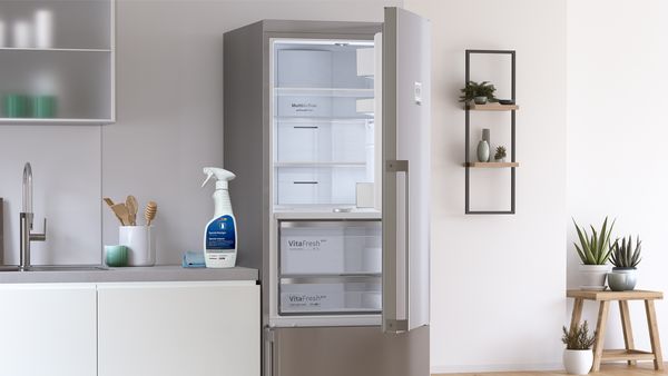 Halvt åbent, tomt køleskab og et rengøringsmiddel til køleskabe og en klud på bordpladen.