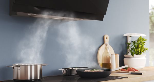 Une casserole et deux poêles sur la table de cuisson à induction Série 6 de Bosch. La vapeur est extraite par la hotte inclinée Série 8 de Bosch.