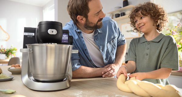  Μια κουζινομηχανή Series 6 πάνω στον πάγκο μιας κουζίνας και δίπλα ένας πατέρας με τον γιο του που χαμογελούν.
