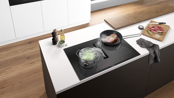 Et billede fra oven af et minimalistisk køkken med induktionskogesektion med emhætte integreret i en køkkenø.