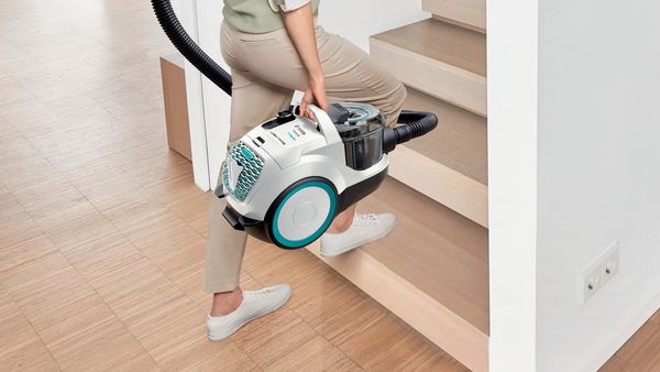 A woman easily carries a lightweight cylinder vacuum up stairs.