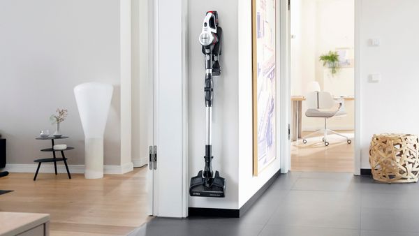 Woman vacuuming up dirt along the edge of the kitchen cabinet with the Unlimited.