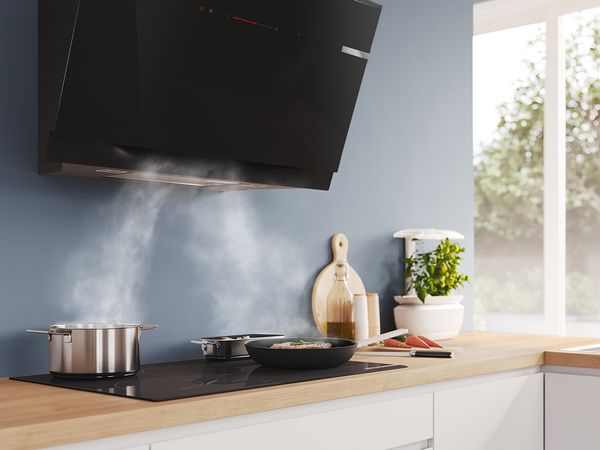 Il vapore viene aspirato da una pentola e da una padella su un piano di cottura verso una cappa da cucina montata a parete.