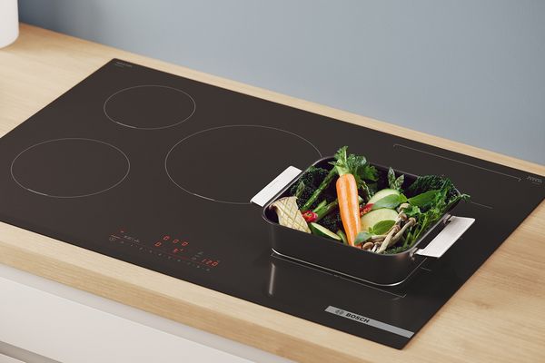 A roasting pan of vegetables sits on an induction cooktop.
