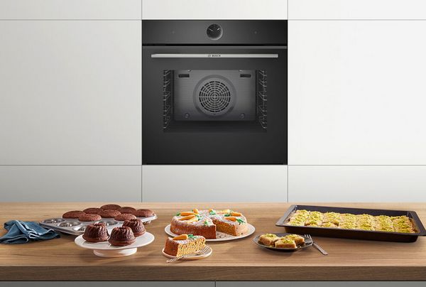 Serie 8 Elektrobackofen von Bosch in einer Küche; auf einer Arbeitsplatte davor stehen verschiedene Backwaren, wie ein Karottenkuchen und Muffins