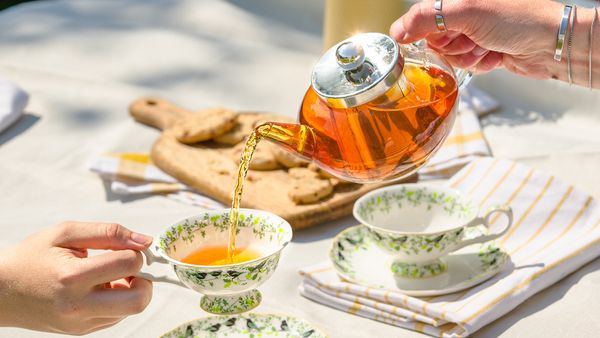 Pouring iced tea from a kettle into a china cup