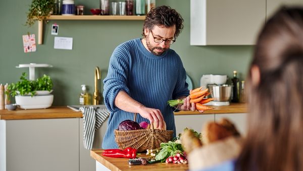 Ein Mann packt in der Küche seinen Einkaufskorb voller Gemüse aus.