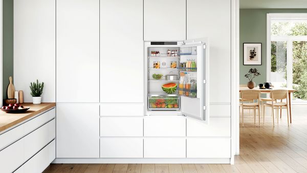 Un mini frigo posizionato tra due mobili bianchi sotto il piano di una cucina.