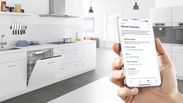 Ręka na pierwszym planie trzymająca smartfon z informacjami o Dziale Obsługi Klienta, na tle nowoczesnej kuchni z otwartą do połowy zmywarką.